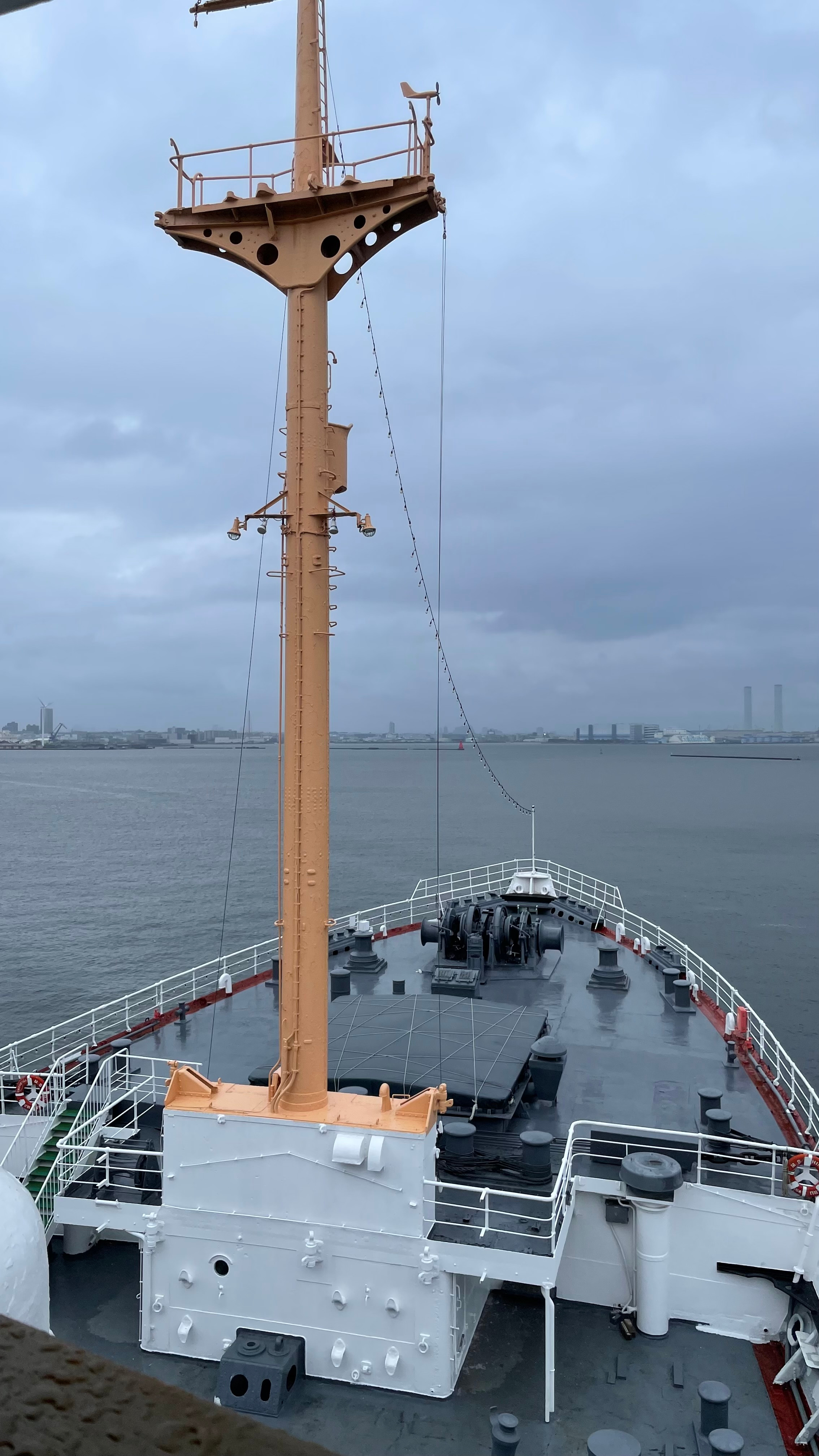 View from the deck of Hikawa Maru looking forward along the bow, with the ship's mast and Yokohama harbor in the background